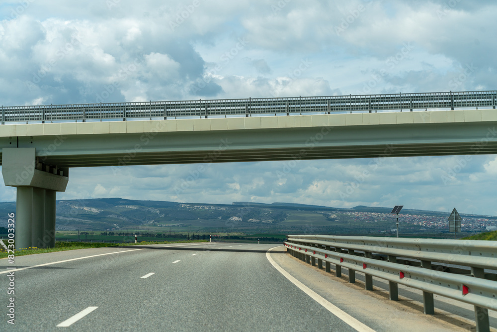 A bridge spans a road with a clear sky above. The bridge is a large structure that is visible from a distance.
