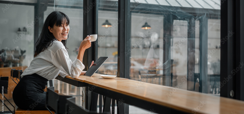 A woman is sitting at a table in a cafe, smiling and holding a cup of coffee. She is also holding a tablet and a laptop, which suggests that she might be working or browsing the internet A woman is sitting at a table in a cafe, smiling and holding a cup of coffee. She is also holding a tablet and a laptop, which suggests that she might be working or browsing the internet