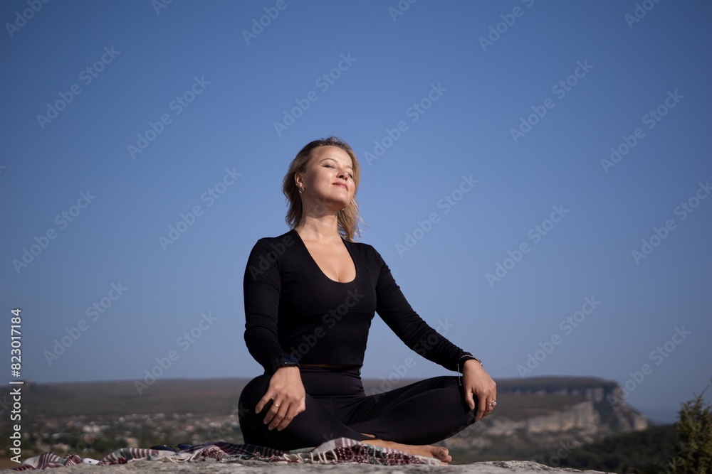 A woman is sitting on a rock with her legs crossed and her hands on her knees A woman is sitting on a rock with her legs crossed and her hands on her knees