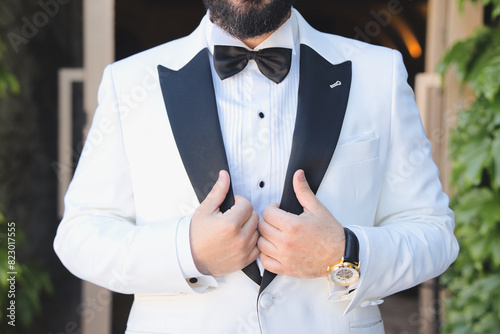фотографія Close-up of hands with bitten nails of an unrecognizable nervous and elegant groom in formal suit, adjusting white suit jacket outdoors