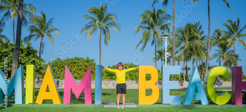 Kid near Miami Beach sign. Kid enjoy summer vacation holiday. Travel, childhood happiness concept. Summer Holiday at Miami Beach Florida. Blond little kid boy having fun on Miami beach, Ocean drive.