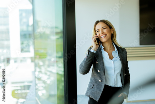 Young professional woman talking on mobile phone by office window on a sunny day