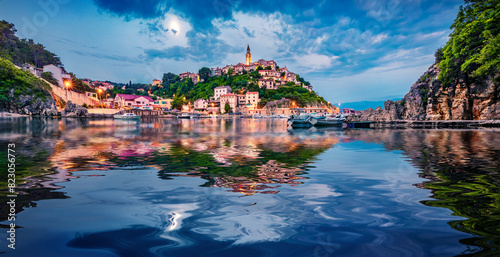 Illuminated old building of Vrbnik  port reflected in the calm waters of Adriatic sea. Picturesque summer seascape of Krk island, Kvarner bay archipelago, Croatia, Europe. Travel the world..