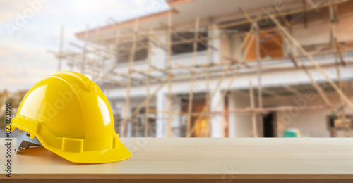 Yellow safety construction helmet on wood table with construction site background