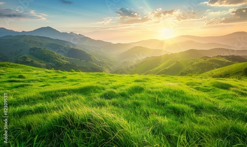 A beautiful green grassy hilltop with the sun setting behind mountains in the background