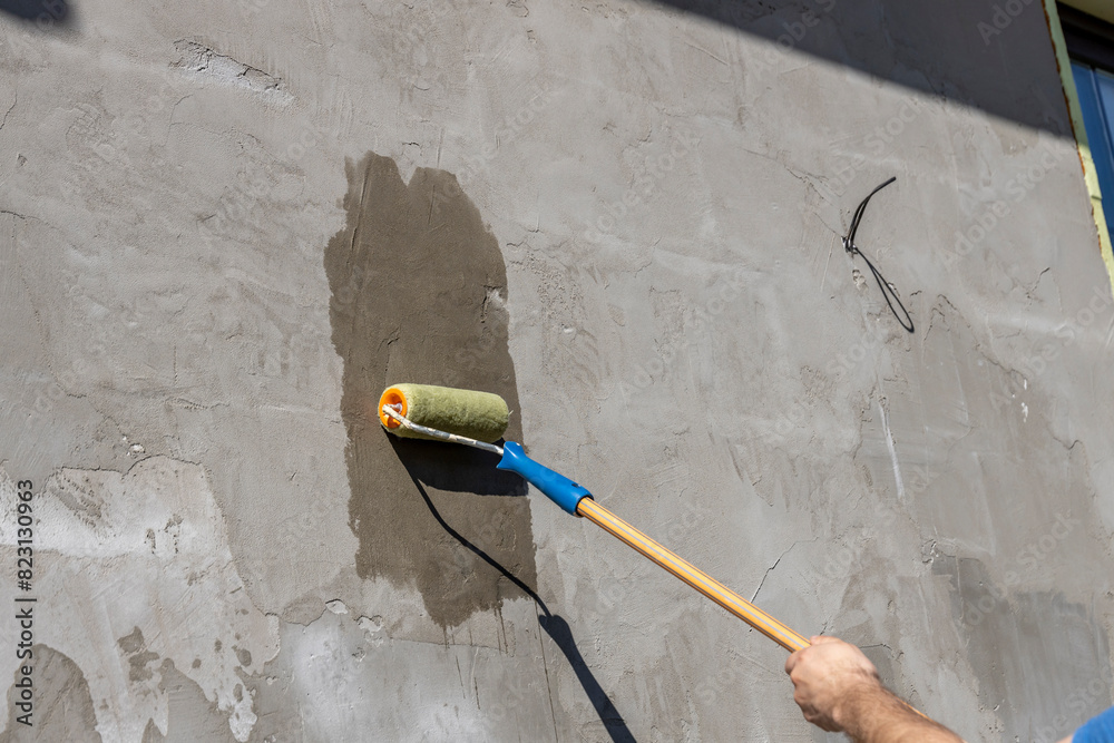 applying a primer to the wall with a yellow roller, showing the process of improving and repairing a house with your own hands. applying a primer to the wall with a yellow roller, showing the process of improving and repairing a house with your own hands.