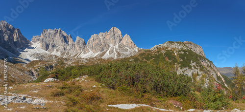 Panorama of rocky ridgesof Croda Rossa di Sesto Mountain in Comelico region with green meadows and blue sky, Dolomites, Italy