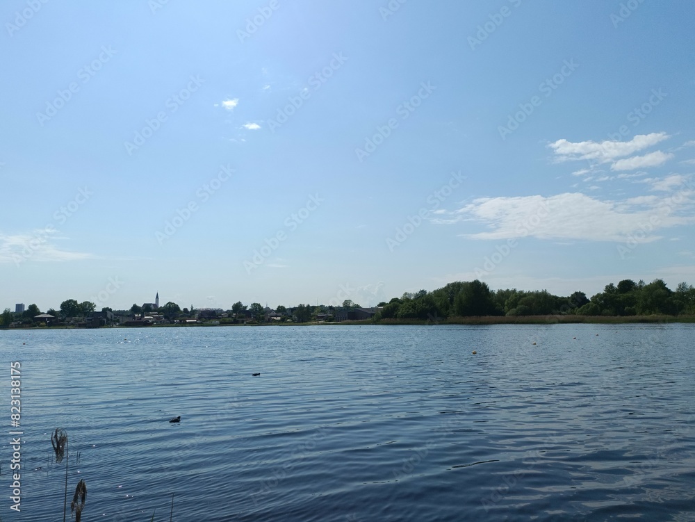 Talsa lake during sunny day. Sunny day. Wavy lake. White and gray colored clouds. Siauliai cathedral and city at the other side of the lake. Horizon over water. Talsos ezeras. Talsa lake during sunny day. Sunny day. Wavy lake. White and gray colored clouds. Siauliai cathedral and city at the other side of the lake. Horizon over water. Talsos ezeras.