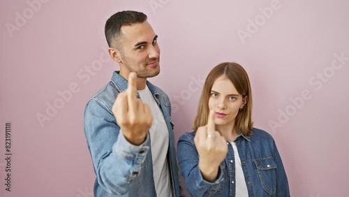 Provocative beautiful couple standing, wearing denim shirts, showing a rude middle finger 'fuck off' gesture, expressing impolite concept over an isolated pink background. photo