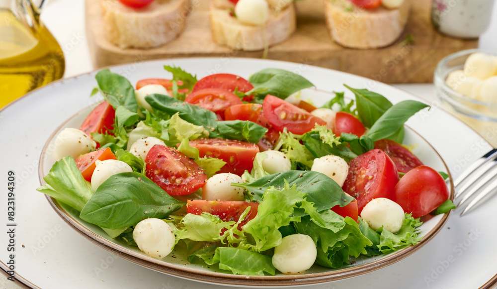 Salad with mozzarella, cherry tomatoes and green lettuce in a white round plate on the table