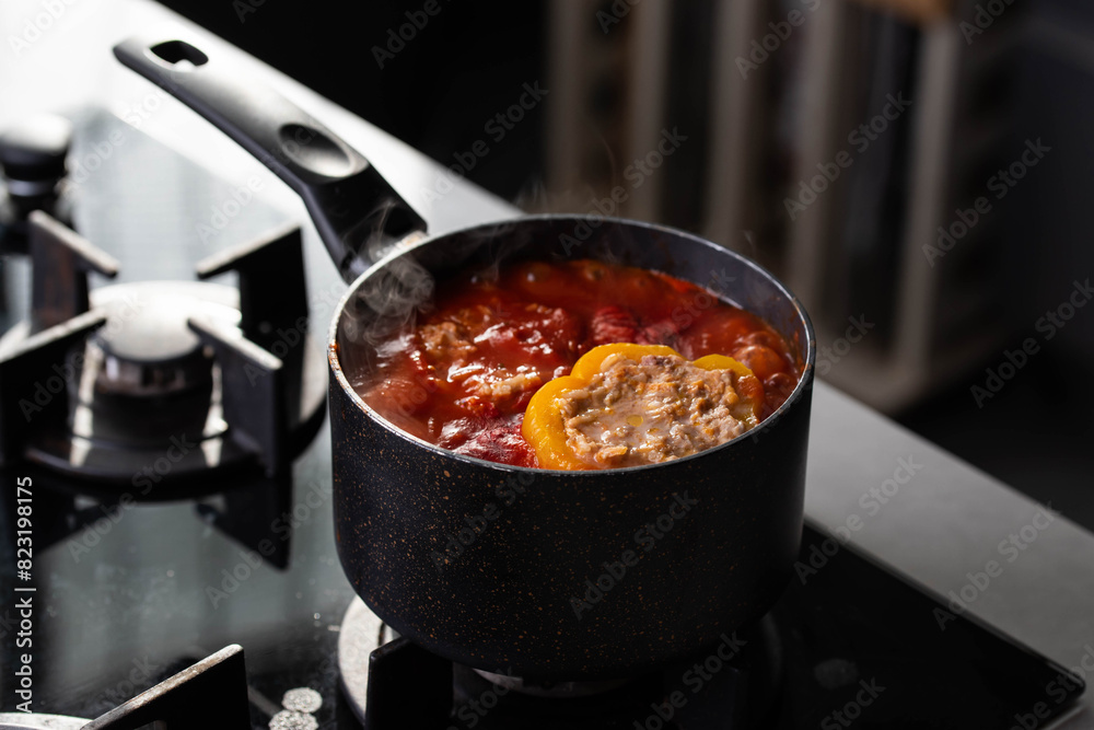 Stuffed peppers with meat and rice cooking in a pot on the stove in red tomato sauce. Sauce is bubbling and steaming, creating a delicious and appetizing food scene. 