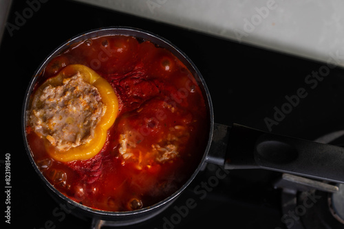 Stuffed peppers with meat and rice cooking in a pot on the stove in red tomato sauce. Sauce is bubbling and steaming, creating a delicious and appetizing food scene. 
