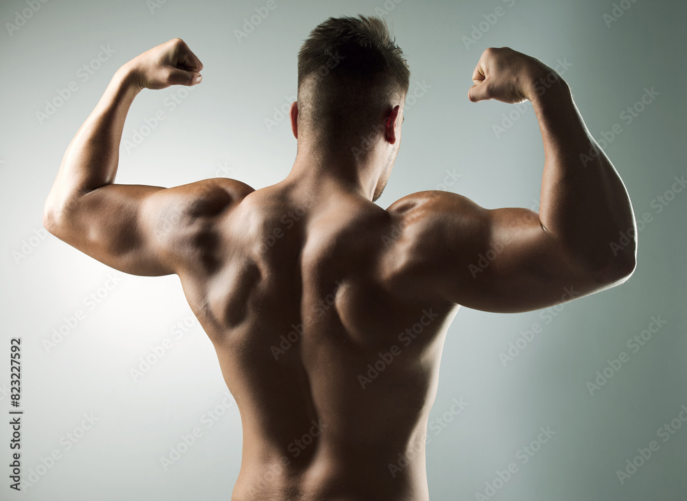 Strong, bodybuilder and flex back with fitness from training progress in studio background. Healthy, man and pride in muscle growth in arms from workout at gym with power and resilience in exercise Strong, bodybuilder and flex back with fitness from training progress in studio background. Healthy, man and pride in muscle growth in arms from workout at gym with power and resilience in exercise