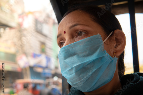 Close up portrait of Indian mature woman sitting in public transport electric auto rickshaw with protective face mask.