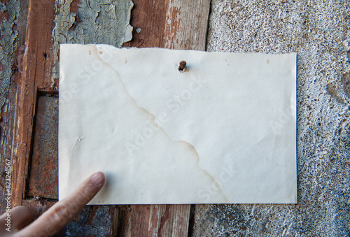 Old vintage paper advertisement hanging on aged wall nailed by rusty doornail with finger pointing on it photo