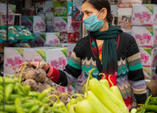 Indian mature woman wearing protective face mask and buying vegetables from outdoor market 