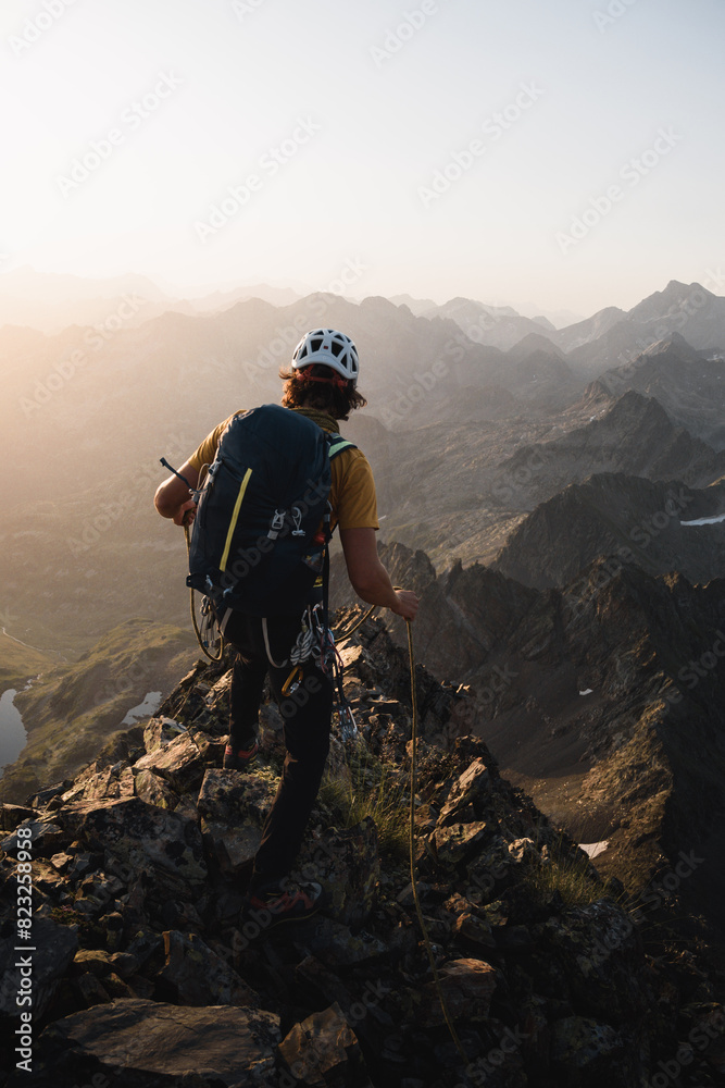 Obraz premium Young mountaineer with a backpack walking along a rocky ridge in the Pyrenees while climbing or mountaineering at sunrise