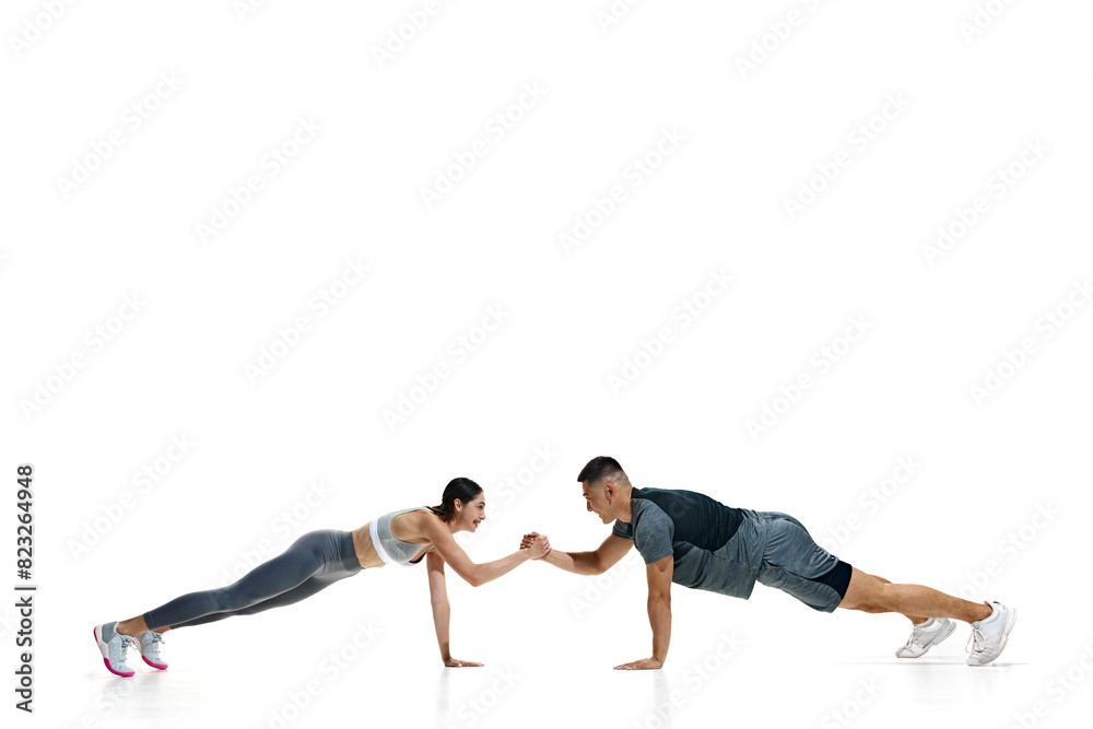 Obraz premium Man and woman in plank position, in friendly arm wrestling match while maintaining their balance against white studio background. Concept of people in sport, healthy lifestyle, teamwork, motivation.