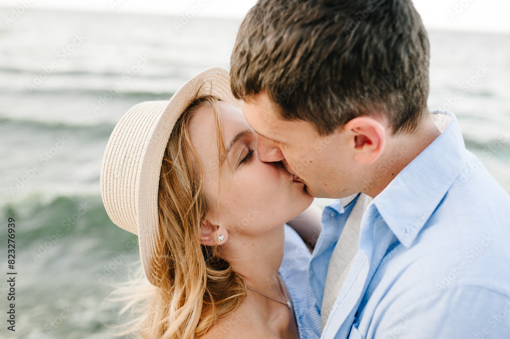 Couple in love hugging and kissing each other on seashore. Man and woman standing on sand sea. Side view. Female and male kisses on beach ocean and enjoy sunny summer day. Spending time together. Couple in love hugging and kissing each other on seashore. Man and woman standing on sand sea. Side view. Female and male kisses on beach ocean and enjoy sunny summer day. Spending time together.