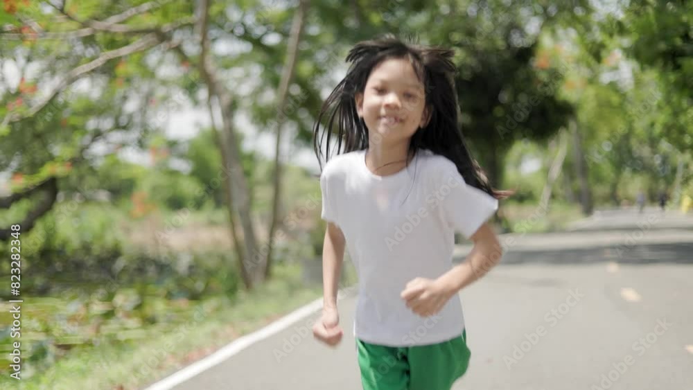 Asian Thai kid girl, aged 8 to 10 years, cute and beautiful face. She is jogging in the outdoor park. She is a girl with a good figure and is tall. Exercise makes her strong. background is green tree. Asian Thai kid girl, aged 8 to 10 years, cute and beautiful face. She is jogging in the outdoor park. She is a girl with a good figure and is tall. Exercise makes her strong. background is green tree.