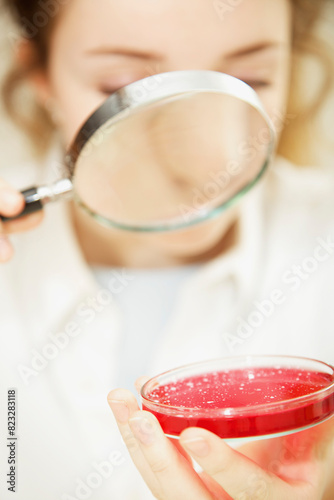 Schoolgirl Examining Cell Culture in Petri Dish with Magnifying Glass
