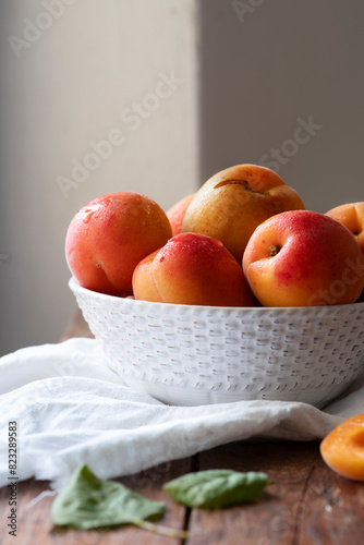 Ripe sweet apricots in a white bowl, on a wooden surface.