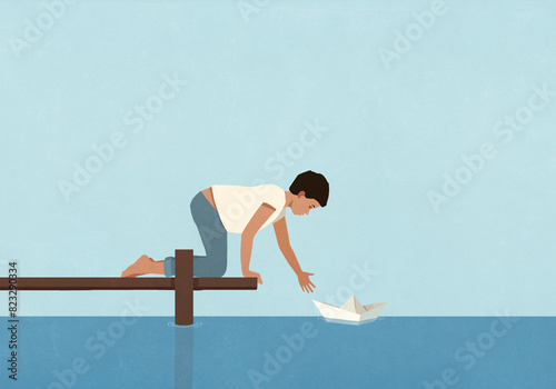 Boy at edge of dock floating paper boat on water
 photo