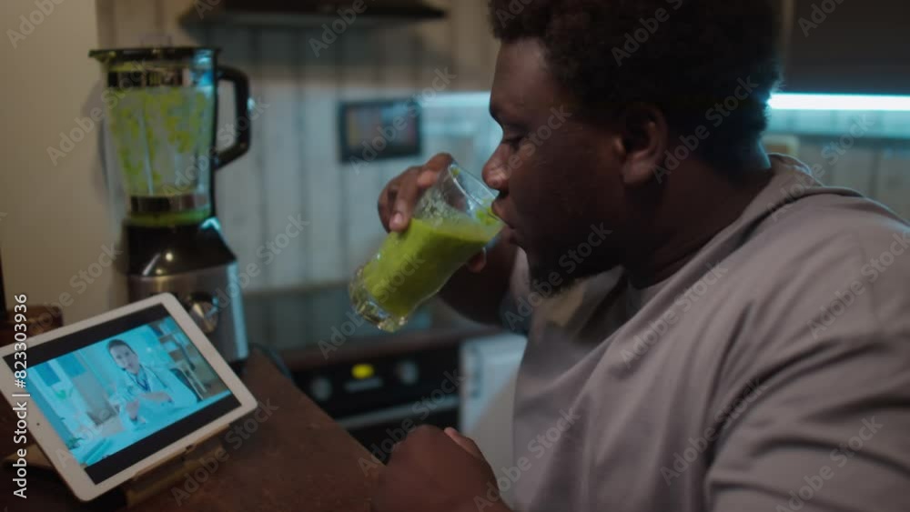 Obese African American man sitting in kitchen at home, drinking green smoothie and discussing weight loss plan with dietician during online consultation via web call Obese African American man sitting in kitchen at home, drinking green smoothie and discussing weight loss plan with dietician during online consultation via web call