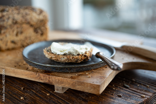 Fresh whole grain bread with cream cheese and dark plate on a wooden cuttingboard. Close-up with short depth of field in front of bright window.