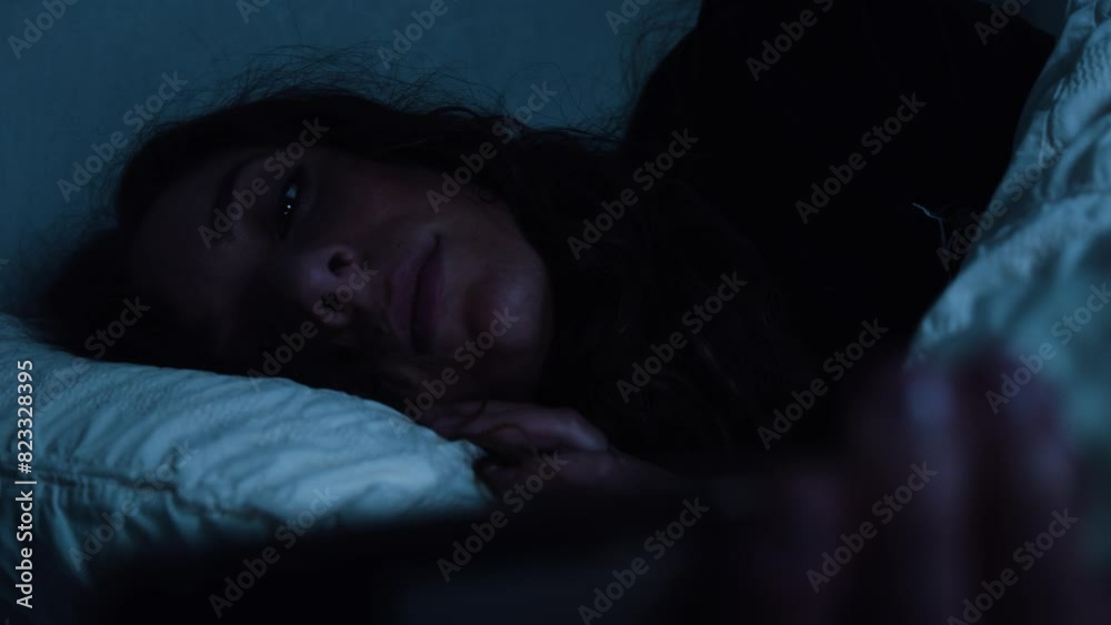 Woman lays in bed whilst using her smart phone late at night Woman lays in bed whilst using her smart phone late at night