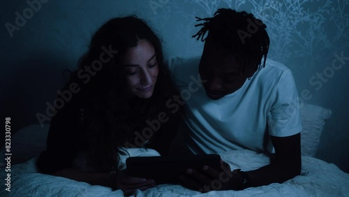 Couple watching a tablet device reacting, nodding and talking while sat in bed at night photo