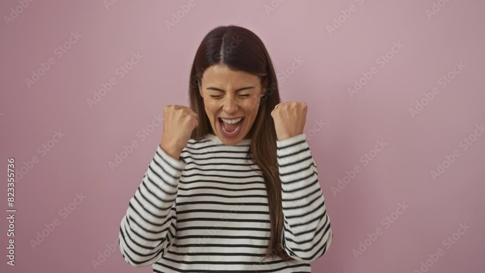Overjoyed, young hispanic woman in striped t-shirt winning, raising arms in victory gesture! isolated on pink, she screams excitedly, her happy face a portrait of success. Overjoyed, young hispanic woman in striped t-shirt winning, raising arms in victory gesture! isolated on pink, she screams excitedly, her happy face a portrait of success.