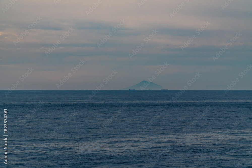 A beautiful coastal area in eastern part of Japan. A clear blue sky and an orange sunrise reflects on the sea water. A big rock formation in the coast line. Island from the distance. A beautiful coastal area in eastern part of Japan. A clear blue sky and an orange sunrise reflects on the sea water. A big rock formation in the coast line. Island from the distance.
