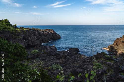 A beautiful coastal area in eastern part of Japan. A clear blue sky and an orange sunrise reflects on the sea water. A big rock formation in the coast line. Island from the distance.