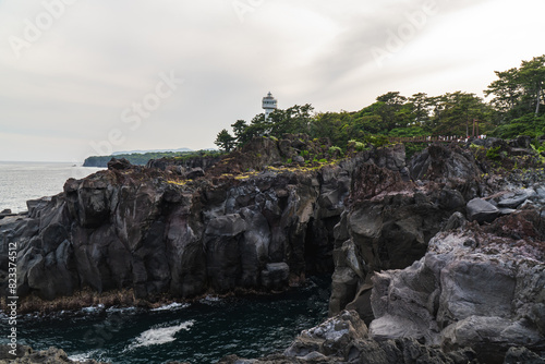 A beautiful coastal area in eastern part of Japan. A clear blue sky and an orange sunrise reflects on the sea water. A big rock formation in the coast line. Island from the distance.