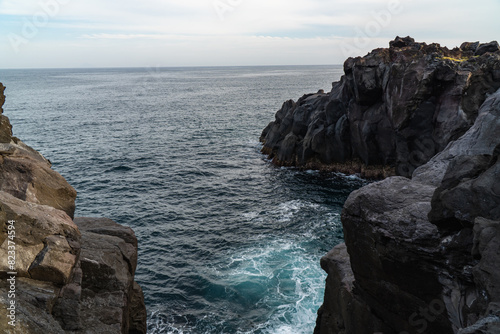 A beautiful coastal area in eastern part of Japan. A clear blue sky and an orange sunrise reflects on the sea water. A big rock formation in the coast line. Island from the distance.