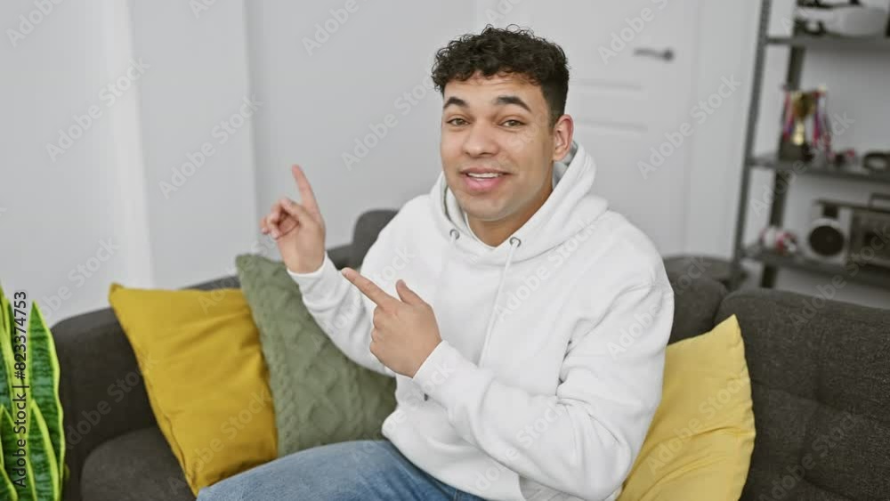 Cheerful young arabian man in casual outfit, joyfully pointing to the side with both hands, smiling and looking at the camera, at home! Cheerful young arabian man in casual outfit, joyfully pointing to the side with both hands, smiling and looking at the camera, at home!