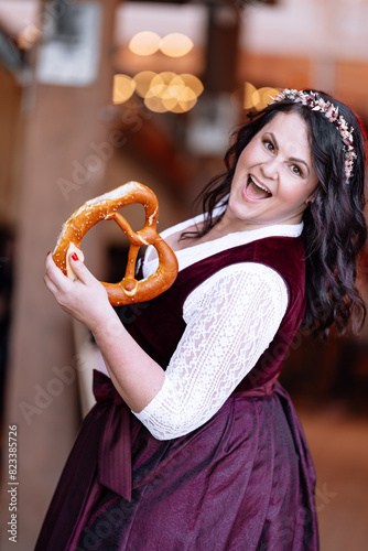 beautiful, young, bavarian woman in traditional costume, dirndl, looking directly into the camera and laughing, holding a pretzel in her hand 