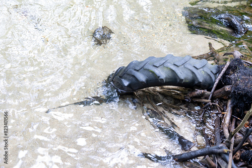 A single discarded tire lies in a clear water stream, highlighting issues of water pollution and environmental neglect