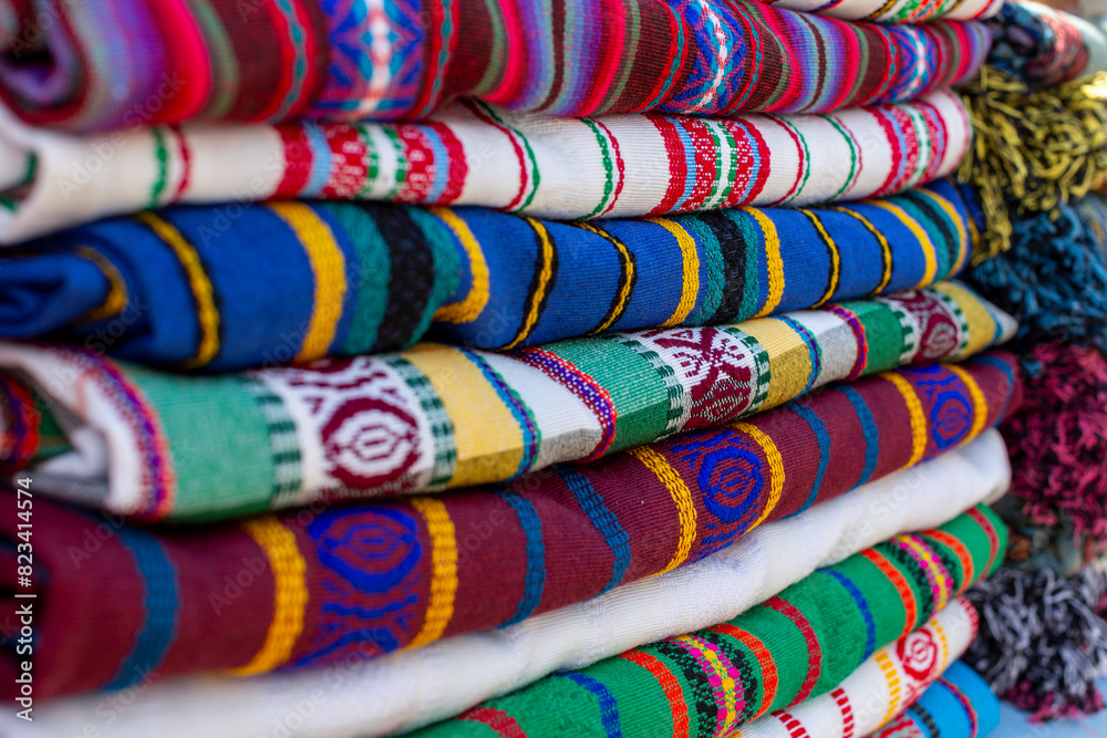 Close up of a pile of traditional, colorful, handmade textiles from El Salvador. Abstract stack of folded fabric, geometric, ethnic, background texture detail. Low angled perspective. Close up of a pile of traditional, colorful, handmade textiles from El Salvador. Abstract stack of folded fabric, geometric, ethnic, background texture detail. Low angled perspective.