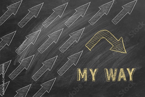 A unique yellow arrow breaks formation against a lot of white arrows on a chalkboard, highlighting the concept of going ones own way and individuality.