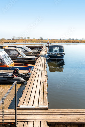 Fishing boats moored at wooden pontoon pier in early morning. Modern motorboats in small docks on calm river. Ships in lake port on spring day