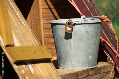 Vintage tin bucket on the edge of a wooden well in the village.                             