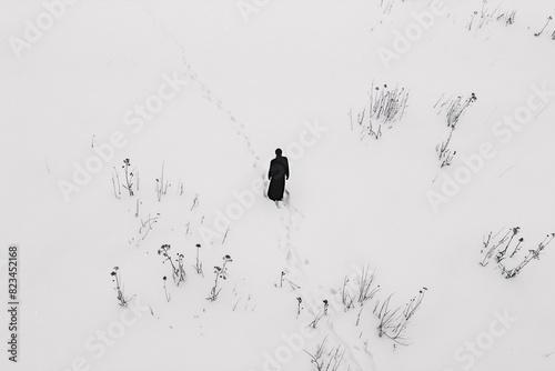 Person in black robe walking through snowy field