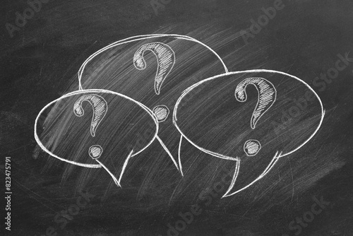 Three chalk-drawn speech bubbles on a blackboard, each containing a question mark. Its a simple yet evocative representation of curiosity and inquiry.