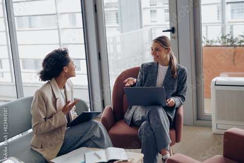 Two young female coworkers talking during business meeting in cozy office. Teamwork concept