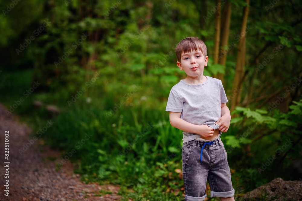 A young boy smiles brightly while standing on a forest path surrounded by lush green foliage and rocks. He is enjoying a peaceful nature walk.