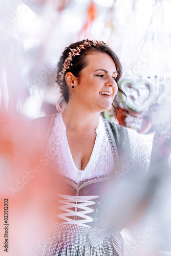 beautiful, young, bavarian woman in traditional costume, dirndl, walks across the oktoberfest with gingerbread heart in front of the gingerbread stall at the oktoberfest