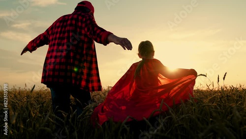 Superheroes daughter of Dad plays in wheat field. Dad child run around in red raincoats, playing outdoors. Family carnival in field, Halloween. Dad, girl dreams of becoming superhero, fly in red cape photo
