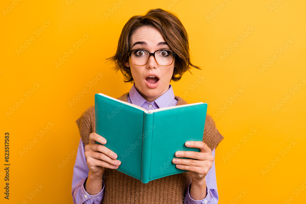 Portrait of speechless impressed woman wear knit waistcoat in glasses read interesting excited book isolated on yellow color background Portrait of speechless impressed woman wear knit waistcoat in glasses read interesting excited book isolated on yellow color background